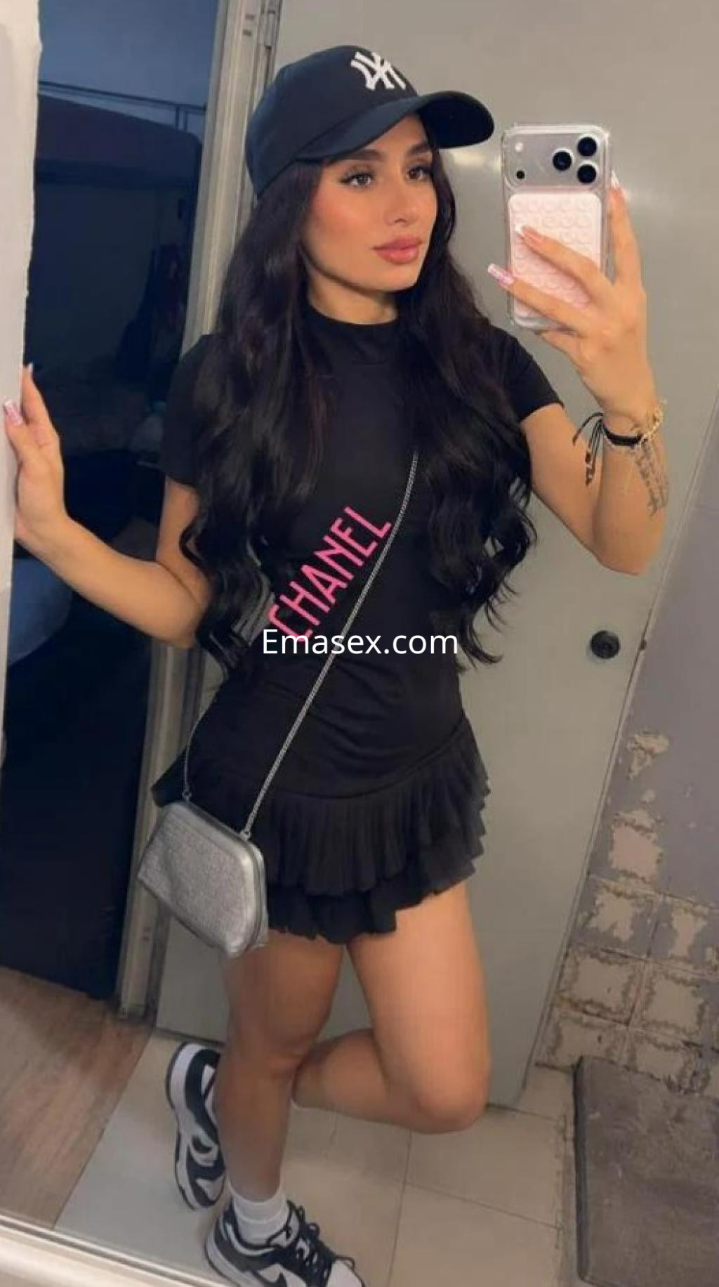 Escort en Barcelona con cabello largo y lacio, vistiendo un vestido negro y gorra, posando para una selfie.