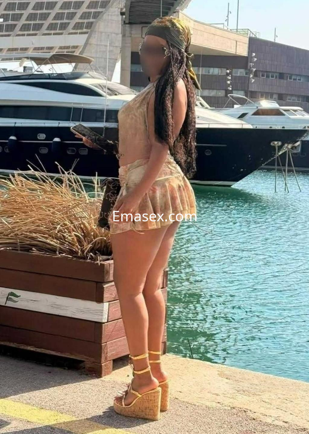 La puta posa en un puerto de Almería, vistiendo un conjunto claro y sandalias de plataforma, con cabello largo.