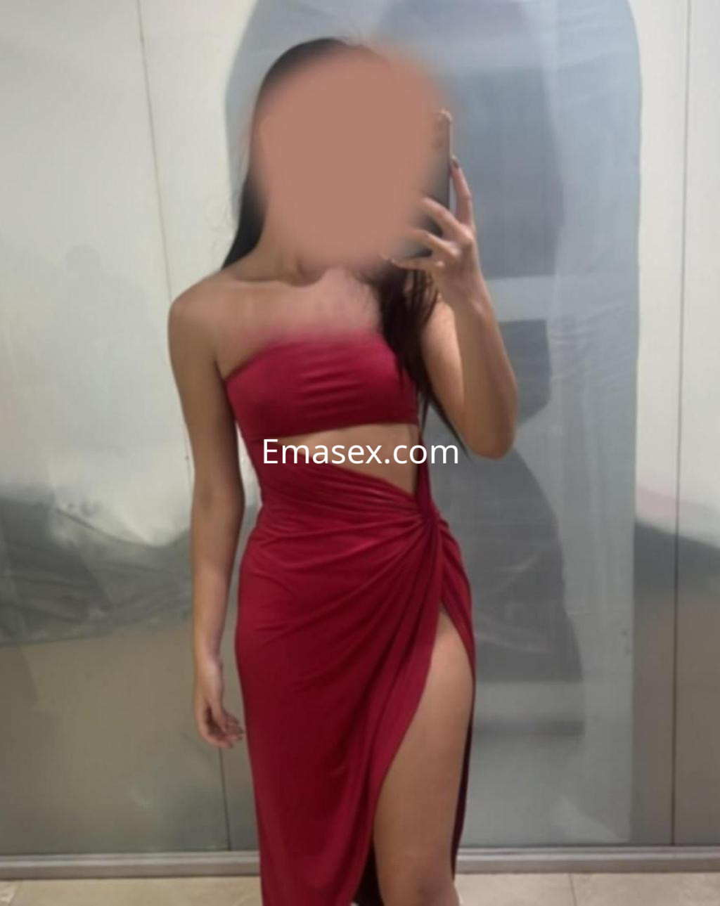Escort en Almería vistiendo un vestido rojo ajustado con abertura lateral, posando frente a un espejo.