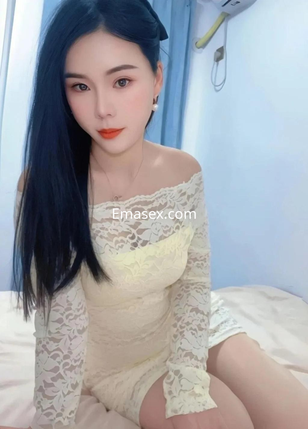 Escort en Tarragona con cabello largo y lacio, vistiendo un vestido de encaje blanco y posando sobre una cama.