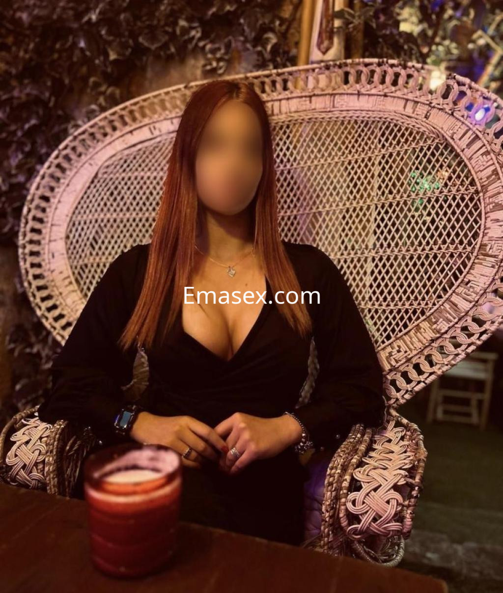 Puta sentada en una silla de mimbre, luciendo un vestido negro y con el cabello largo y lacio en Murcia.