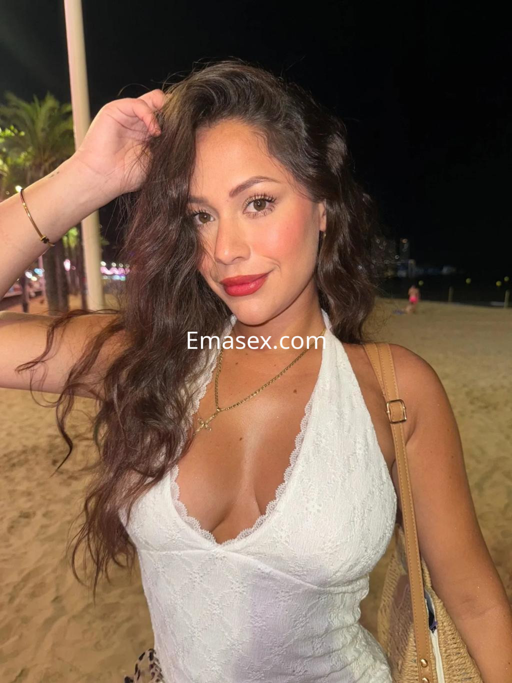 Puta con cabello largo y ondulado, viste una blusa blanca y posa en la playa de Gijón por la noche.