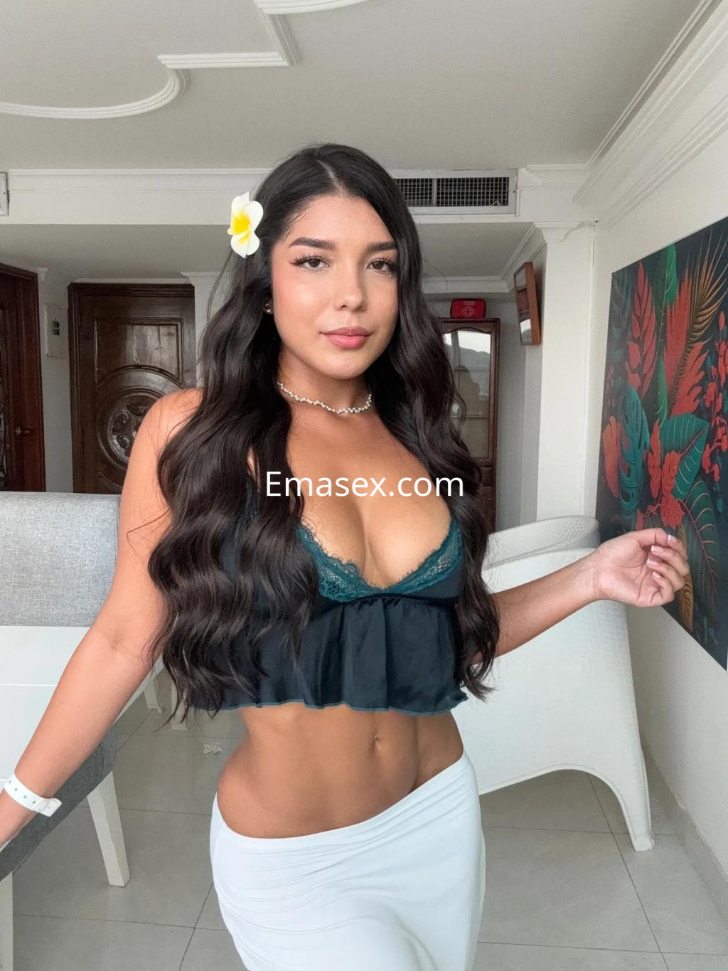 Escort en Sevilla con blusa de encaje verde y falda blanca, sonriendo mientras posa en un ambiente elegante.