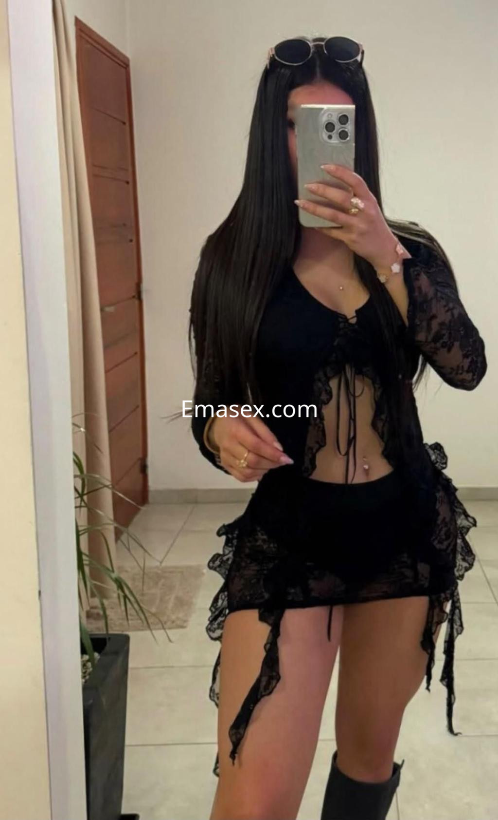 Escort en Toledo luciendo un conjunto de lencería negra con detalles de encaje y botas altas, posando frente al espejo.