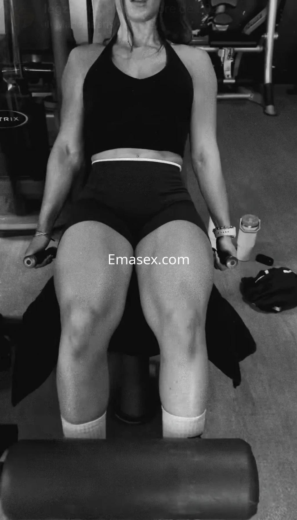 Puta en Toledo realizando ejercicios de piernas en el gimnasio, vistiendo un top negro y shorts cortos.