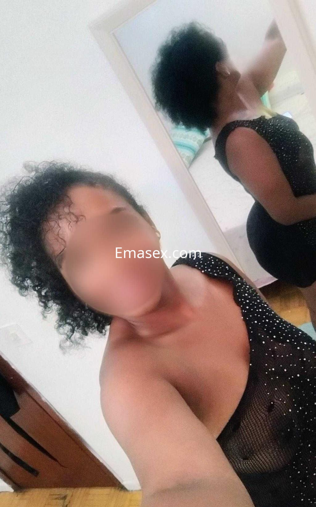 Puta en Pontevedra con cabello rizado y vestido negro transparente, posando frente a un espejo.