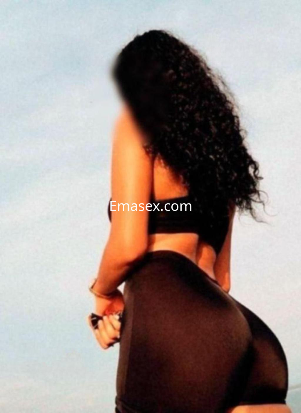 Escort en Almería posando de espaldas, con cabello rizado y atuendo ajustado que resalta su figura.