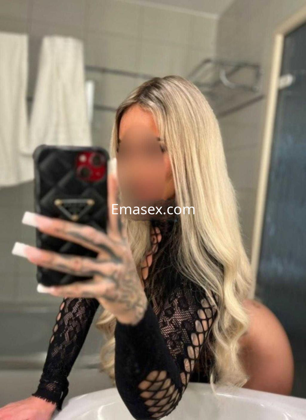Escort en Badajoz con cabello rubio y lacio, vestida con un top negro de encaje, posando en un baño.