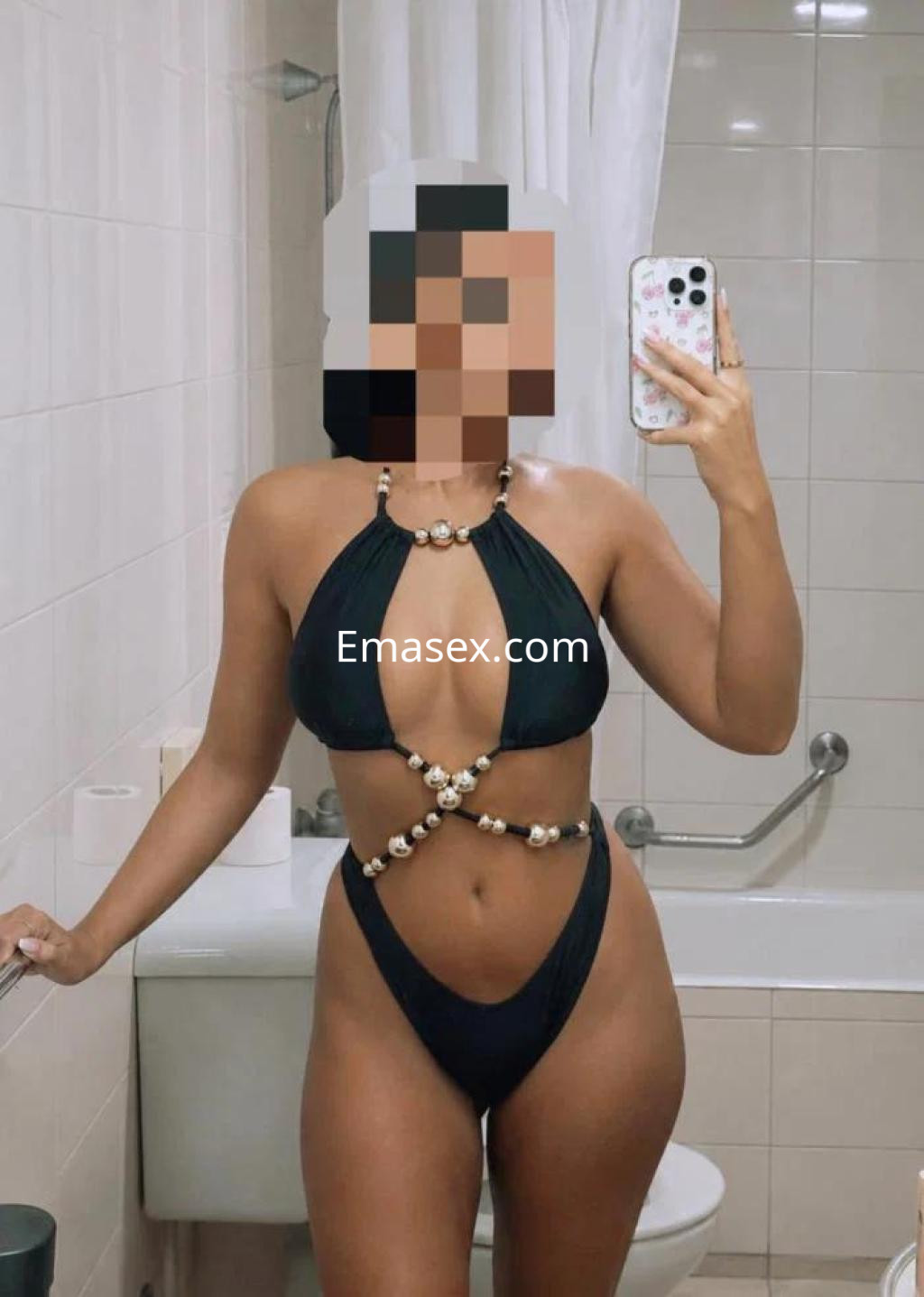 Escort en Pontevedra posa en un baño con un bikini negro que resalta su figura, sosteniendo su teléfono.