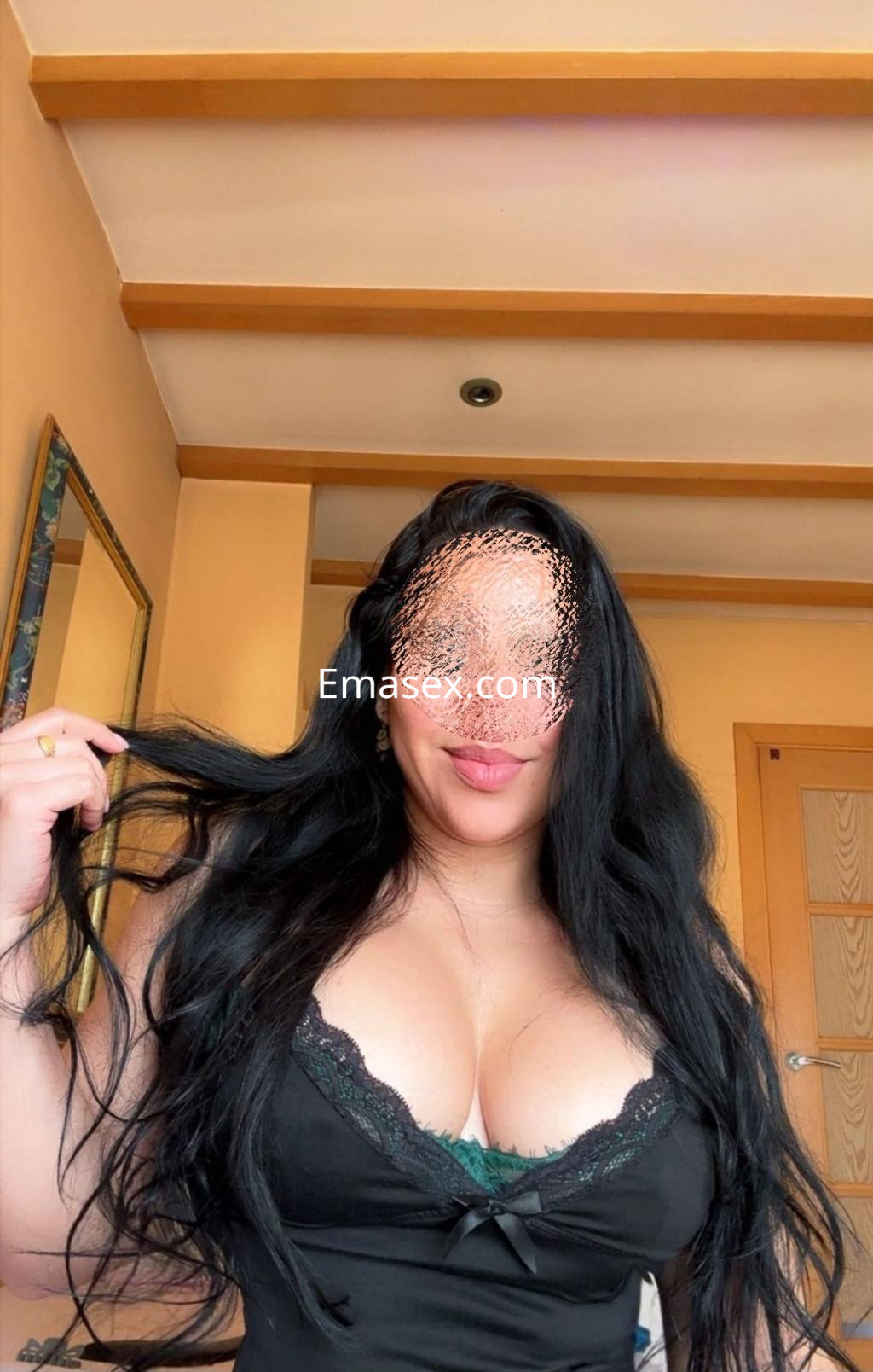 Escort en Vigo con cabello largo y negro, viste una blusa negra con encaje y sonríe mientras se toca el cabello.