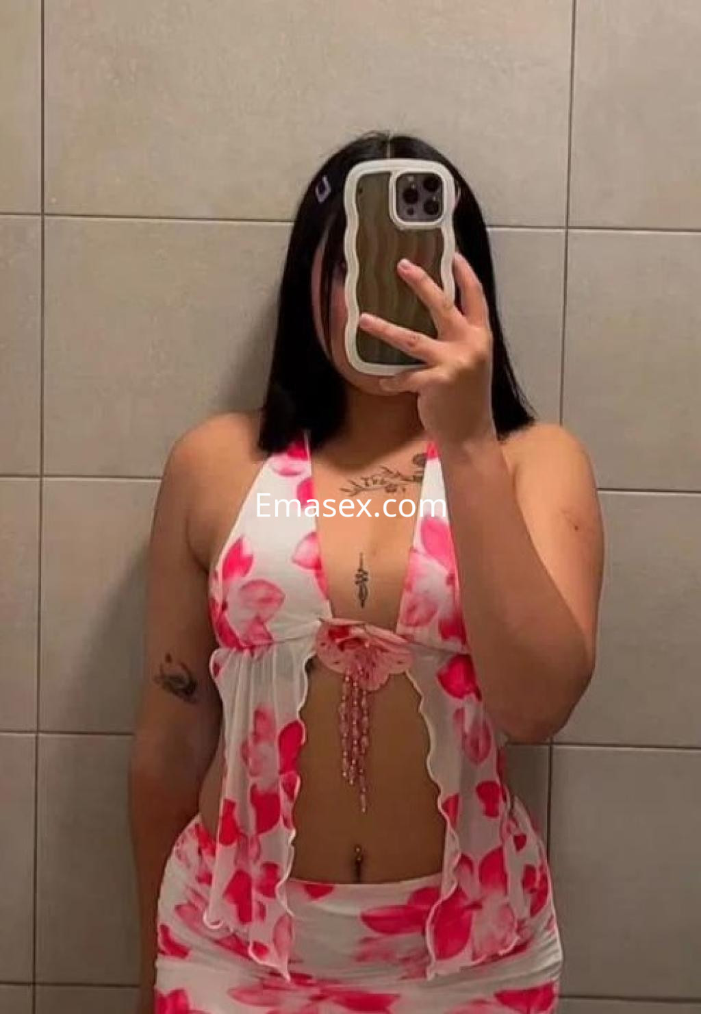 Puta en Madrid posando en un baño con un vestido corto de flores en tonos rosas, mostrando su figura y tatuajes.