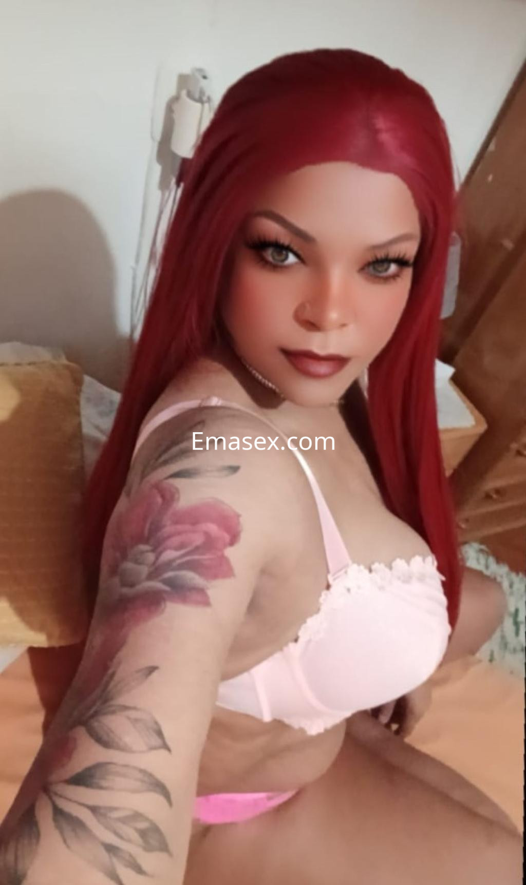 Puta con cabello largo y rojo, vistiendo un sujetador rosa, posa en una cama en Salamanca, mostrando un tatuaje en su brazo.
