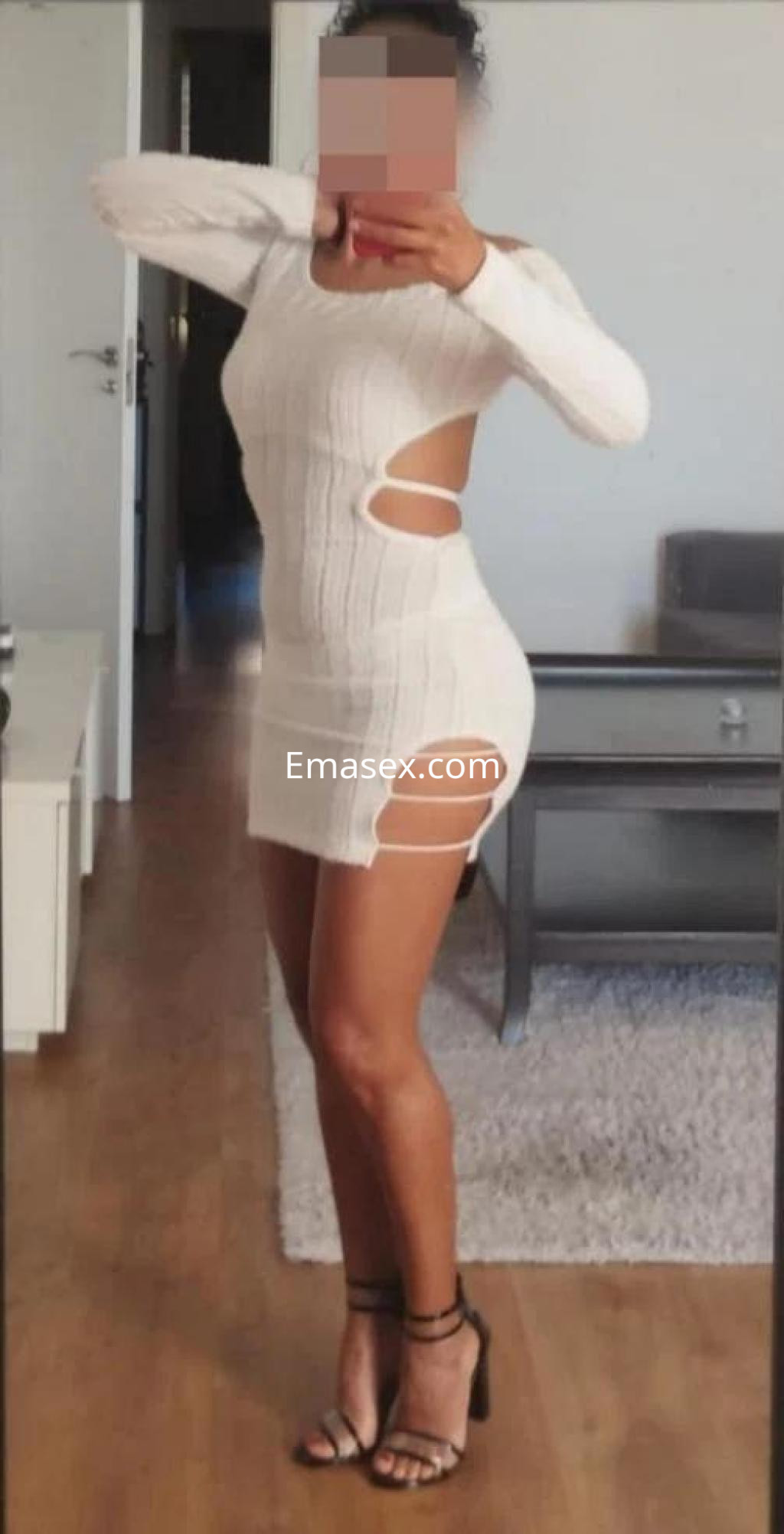 La puta posa en un vestido blanco ajustado con cortes laterales, mostrando sus piernas en Málaga.