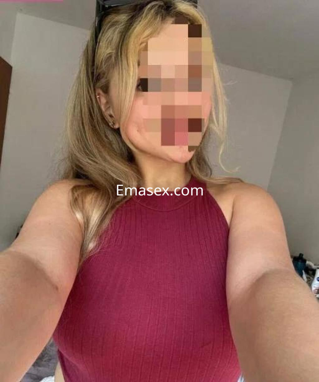 Escort en Coruña con blusa sin mangas de color burdeos, cabello rubio y posando en un entorno interior.