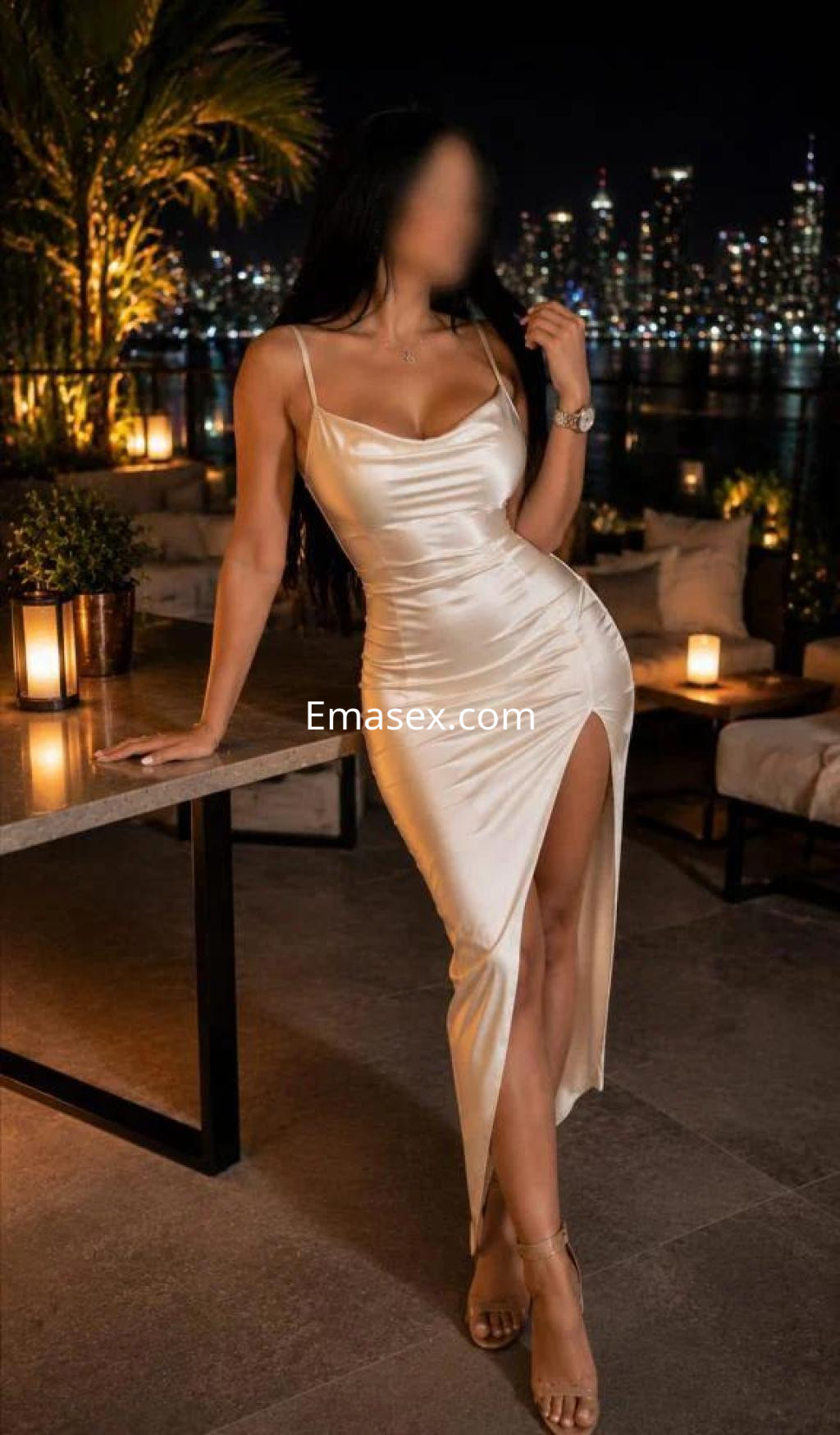 Escort en Madrid con vestido satinado de tirantes, posando junto a una mesa en un ambiente nocturno iluminado.