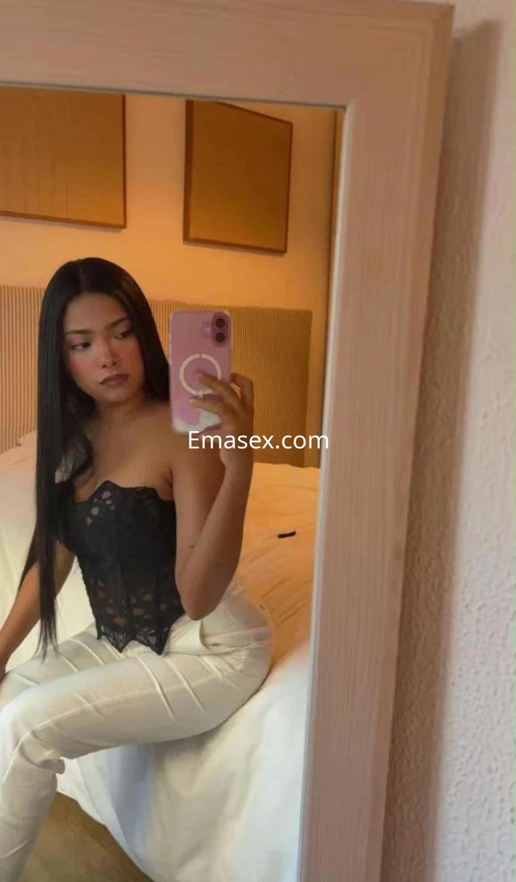 La puta luce un corset negro y pantalones blancos, posando en una habitación con decoración minimalista en Tarragona.