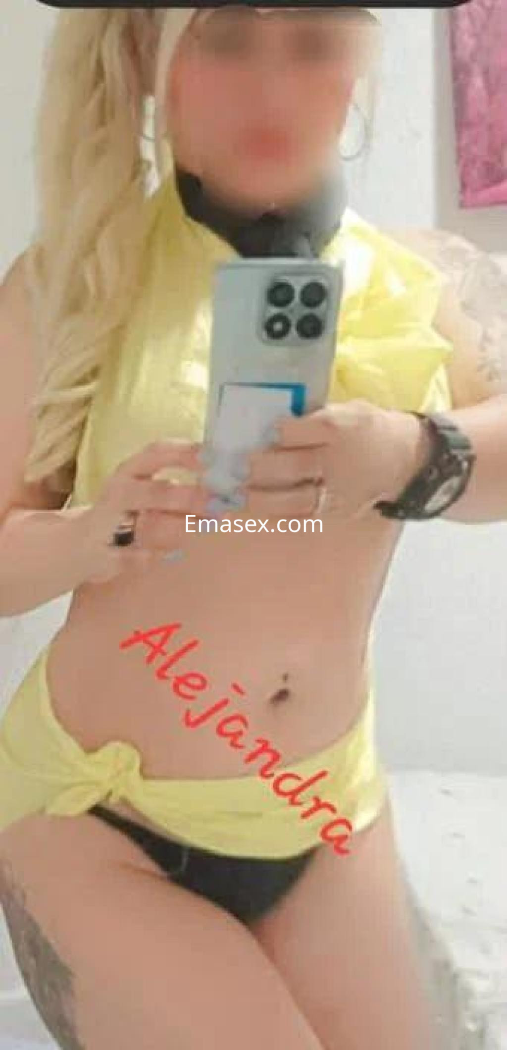 La puta en Sevilla se muestra con un top amarillo y una lencería negra, sosteniendo un teléfono en el espejo.
