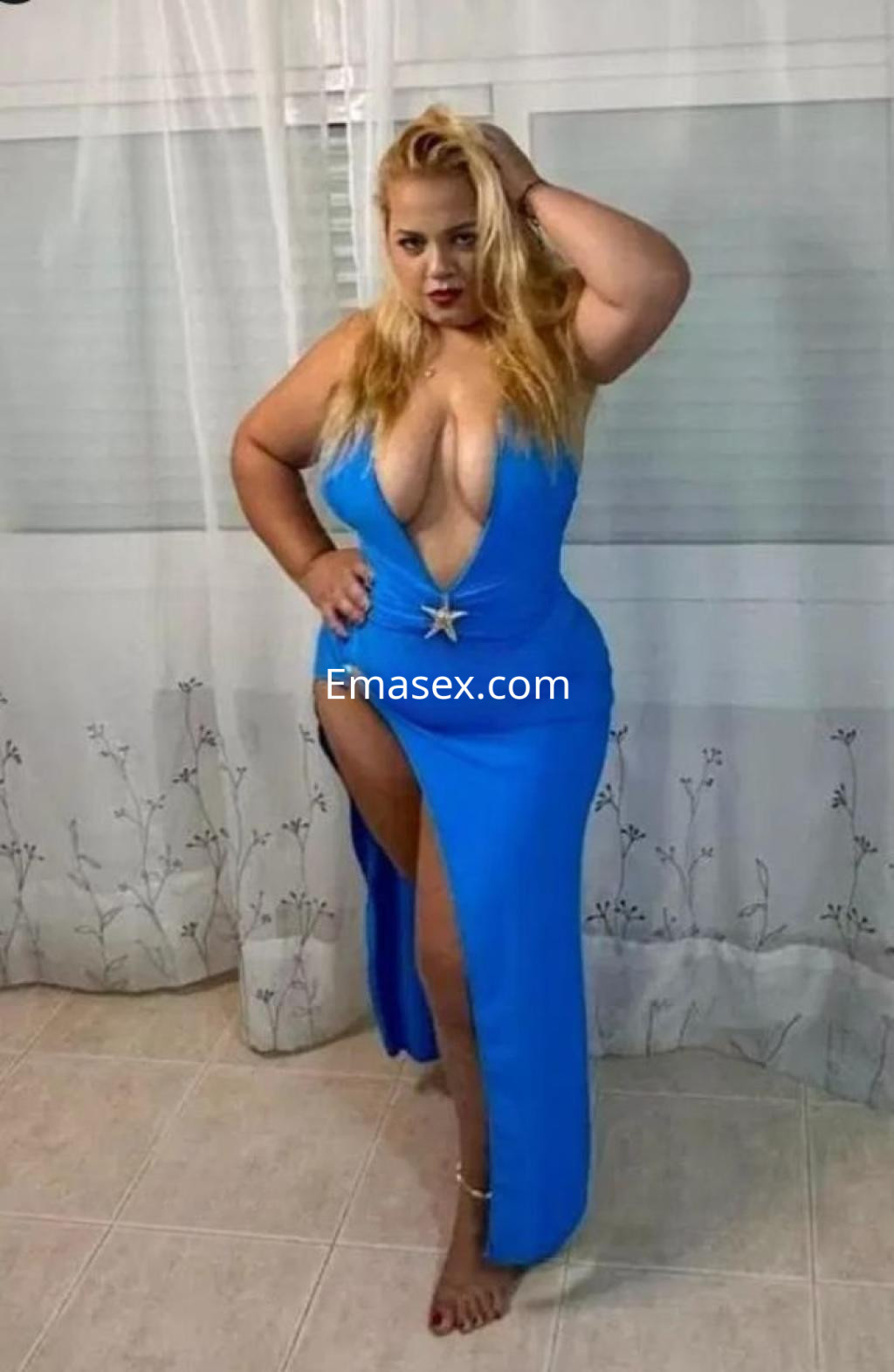 Puta posando en Málaga, viste un vestido azul con escote pronunciado y abertura lateral, cabello rubio.