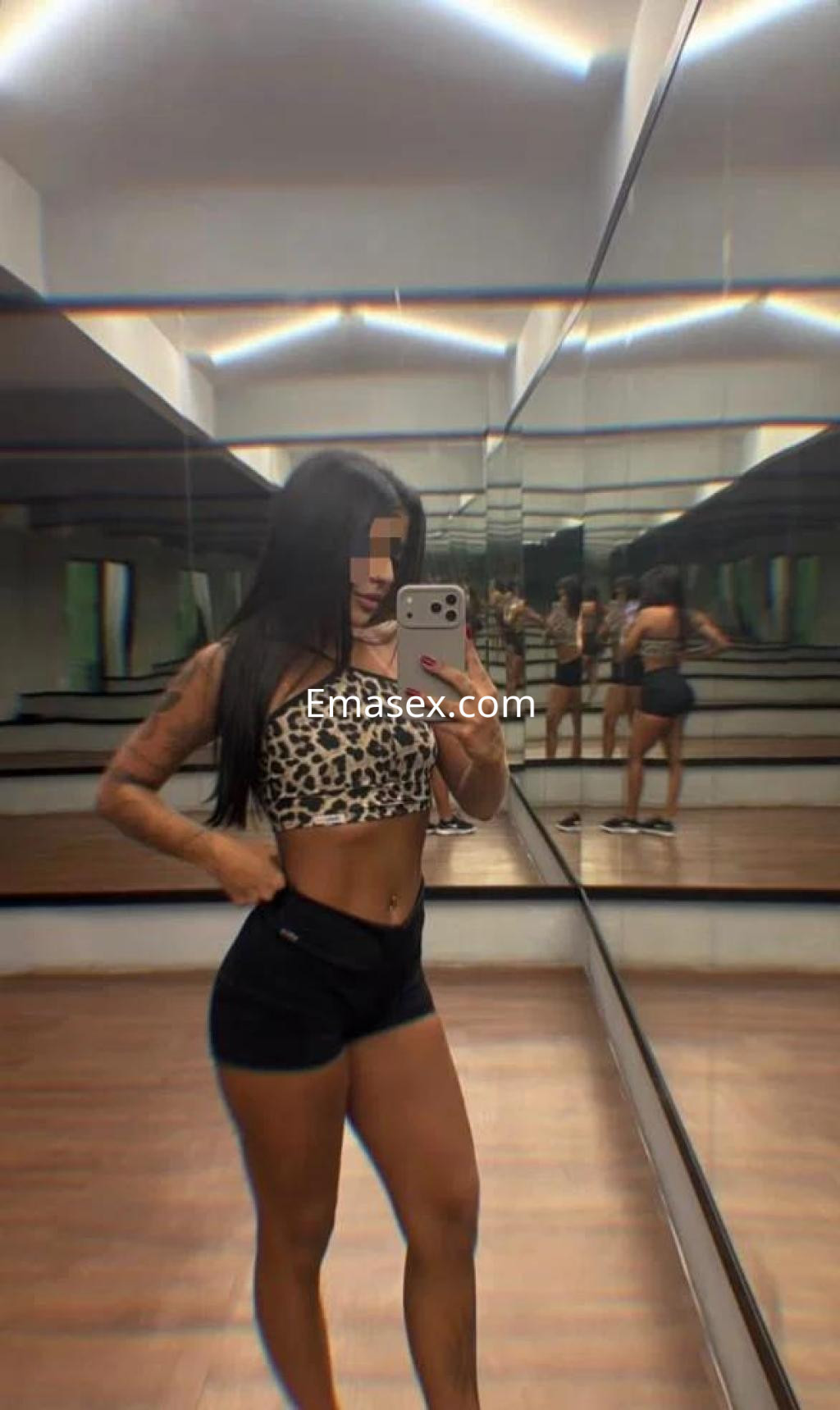 Escort en Málaga con cabello largo y lacio, viste un top de leopardo y shorts negros, posando frente a un espejo.