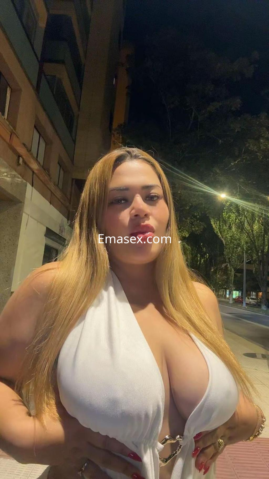 Puta en Pamplona luciendo un vestido blanco ajustado y cabello largo, posando en la calle por la noche.