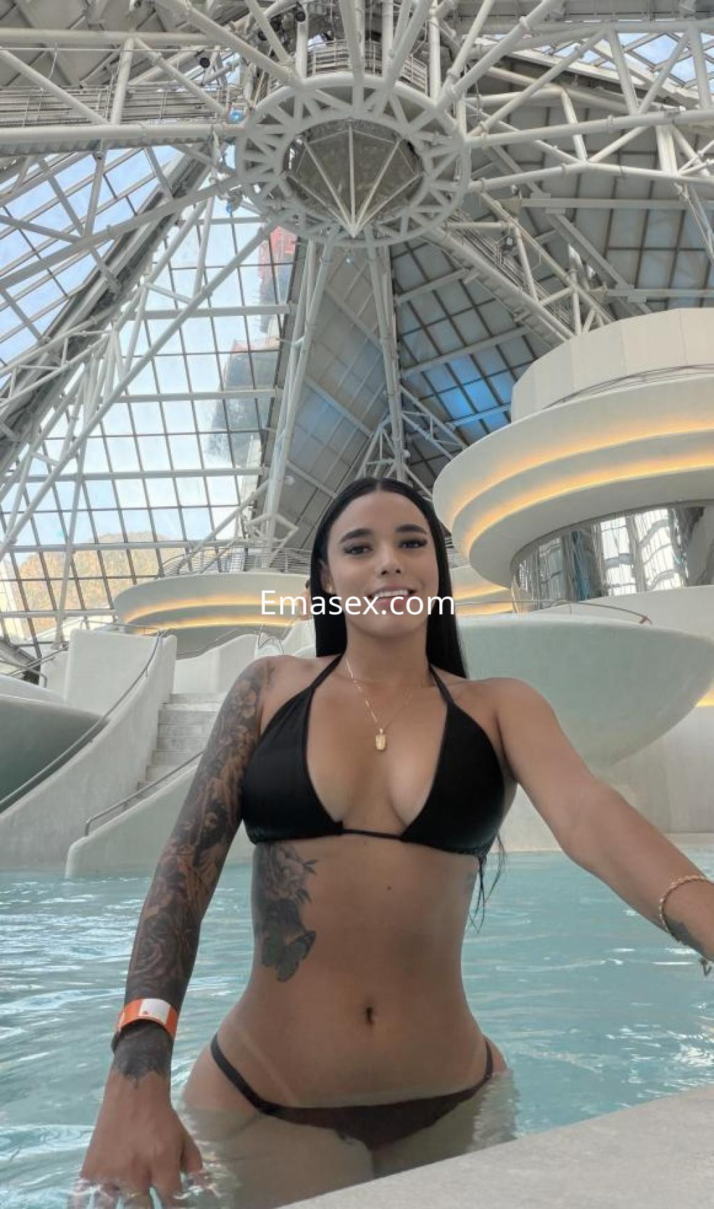 Puta en Lleida, posando en una piscina con un bikini negro, mostrando un tatuaje en el brazo y una sonrisa.