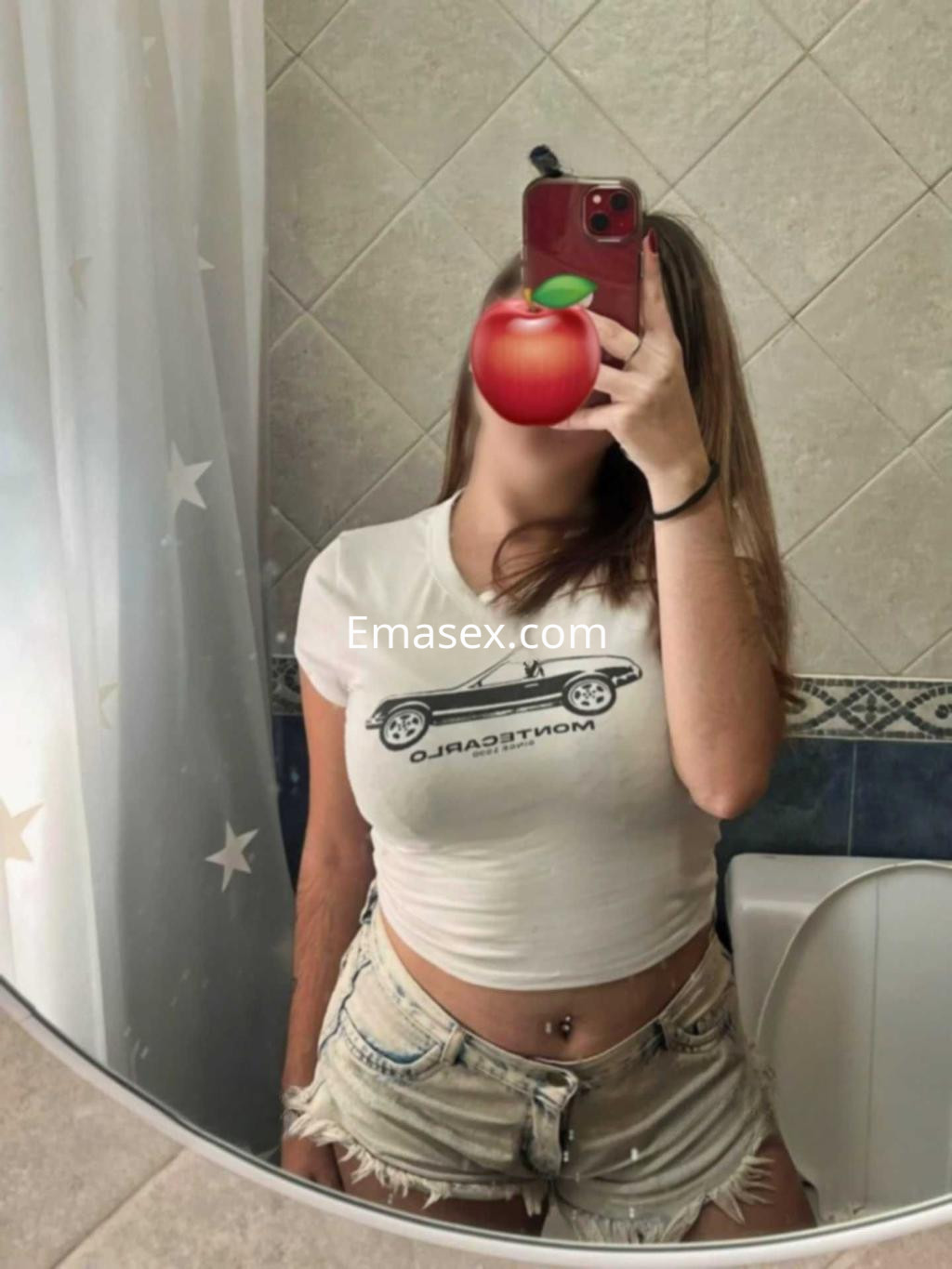 Escort en Granada posando frente a un espejo, viste una camiseta blanca y shorts de mezclilla.