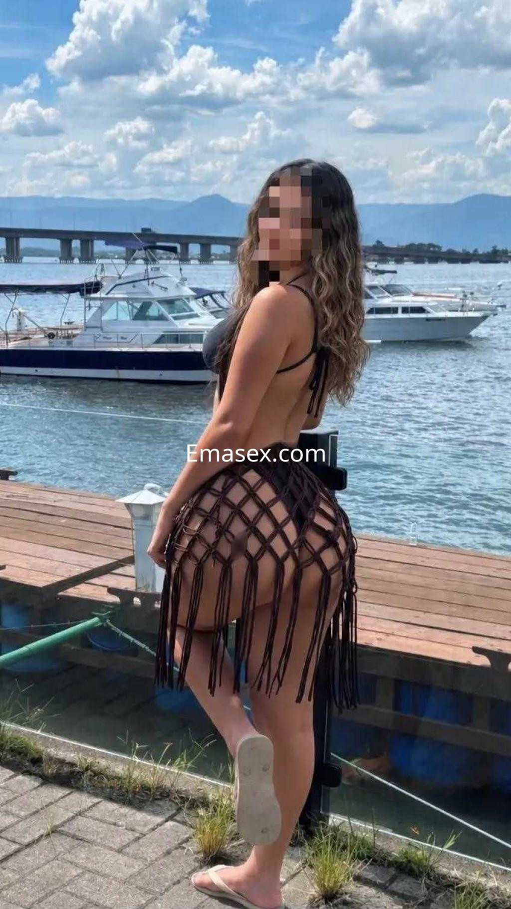 Puta de espaldas en Ibiza, luciendo un bikini negro y una falda de flecos, frente a un paisaje costero.