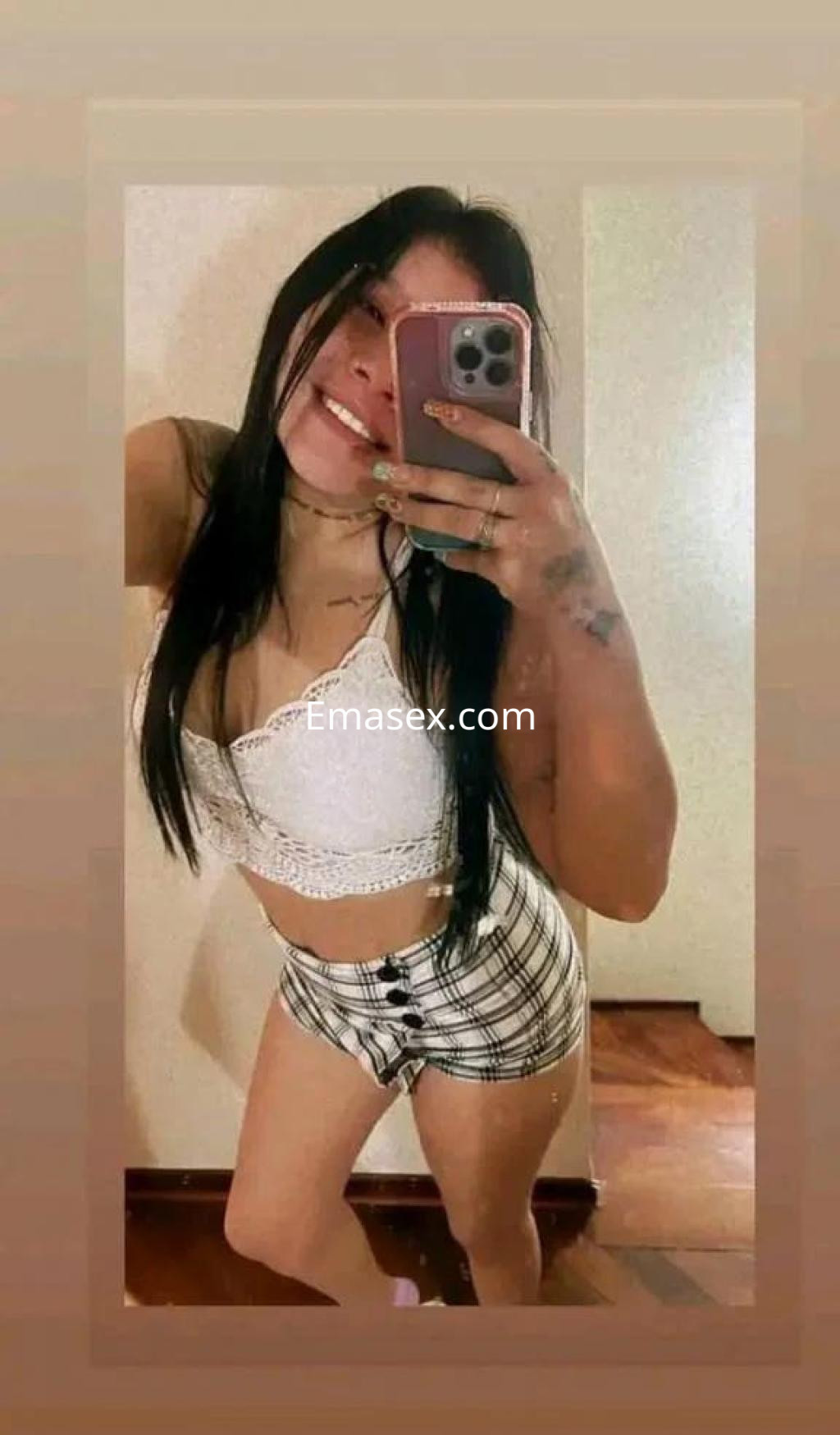 Puta en Zamora sonríe mientras toma una selfie, luciendo un top blanco y shorts cuadros, con cabello largo.