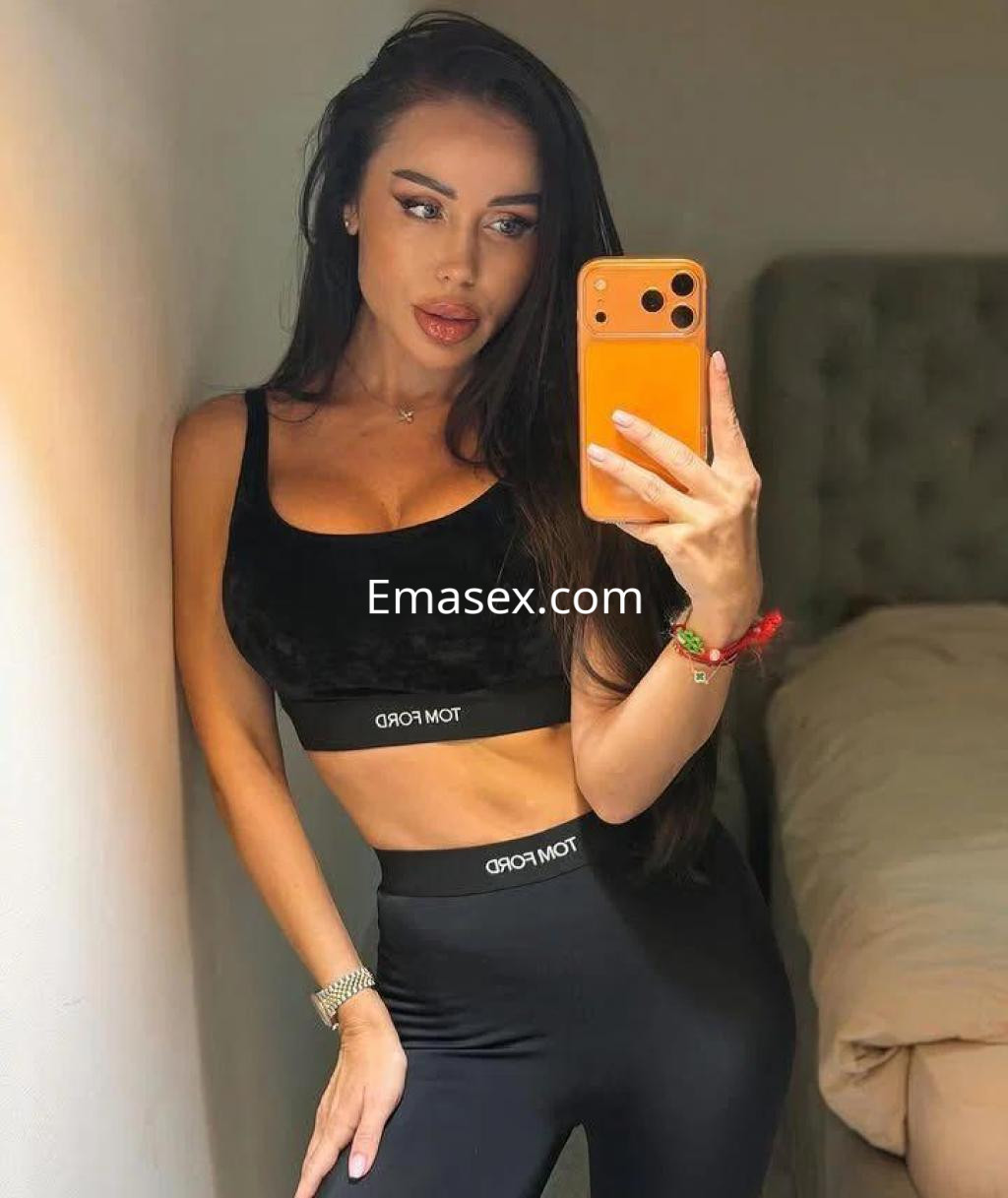 Escort en Alicante posando frente al espejo con top negro y leggins a juego, cabello largo y lacio.