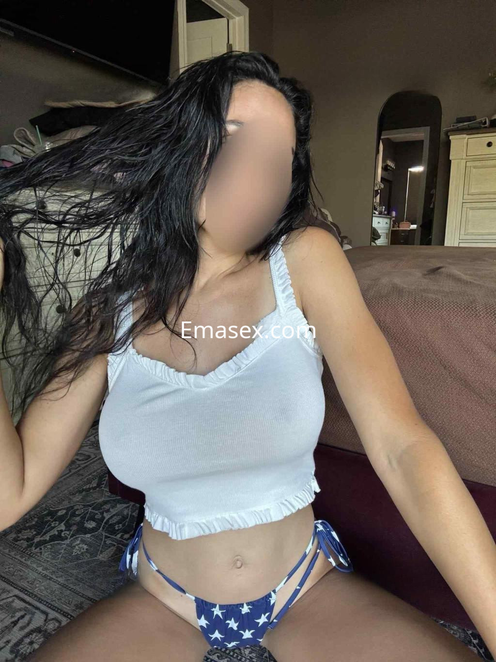 Escort en Alicante posando con una blusa blanca sin mangas y un bikini azul con estrellas, sentada en un sofá.