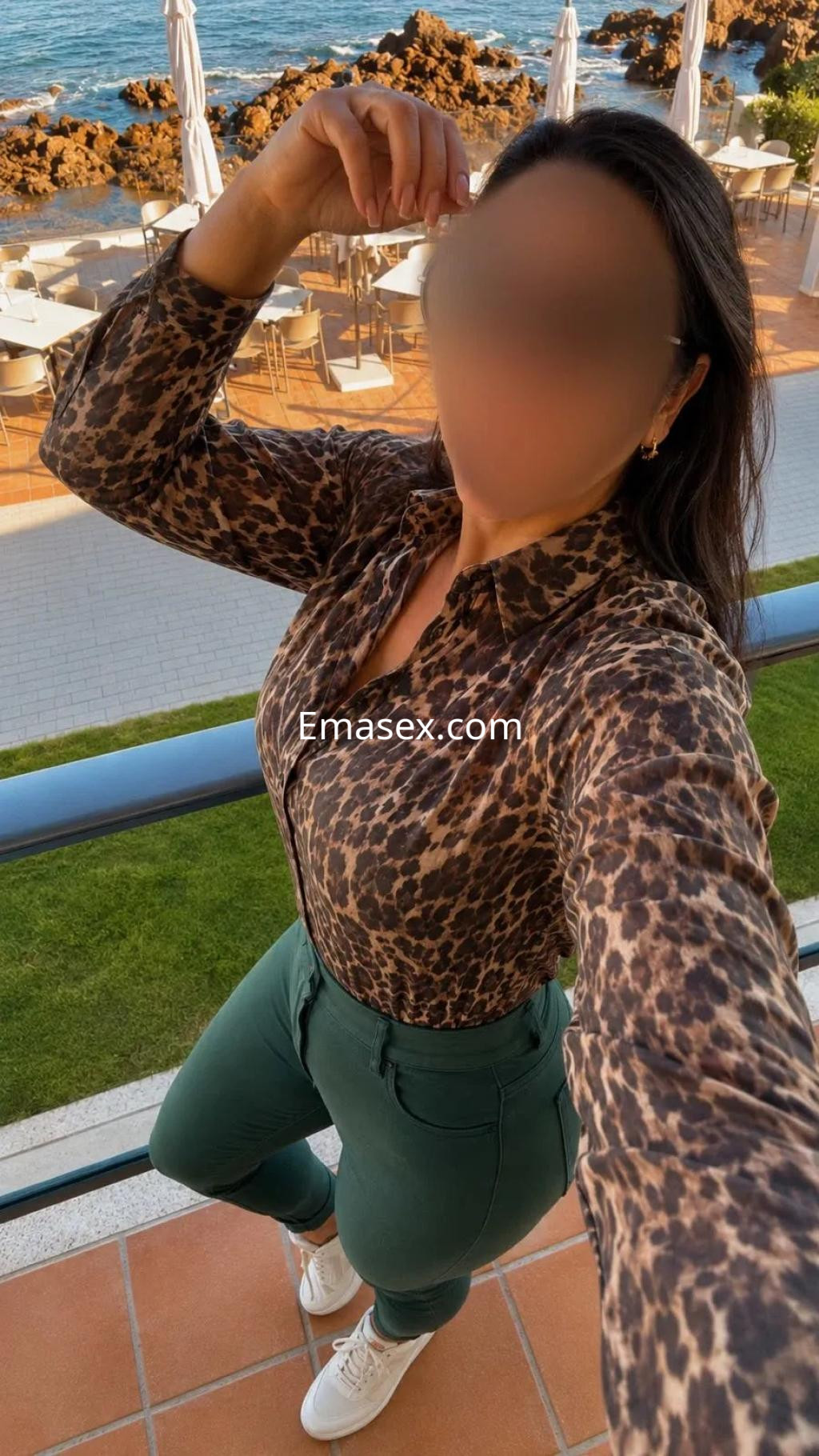 Puta de Zaragoza viste una blusa de estampado animal y pantalones verdes, posando en un entorno al aire libre.