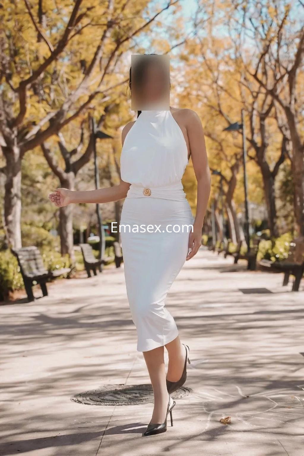 Puta camina con confianza en un parque de Valencia, luciendo un vestido blanco ajustado y tacones altos.