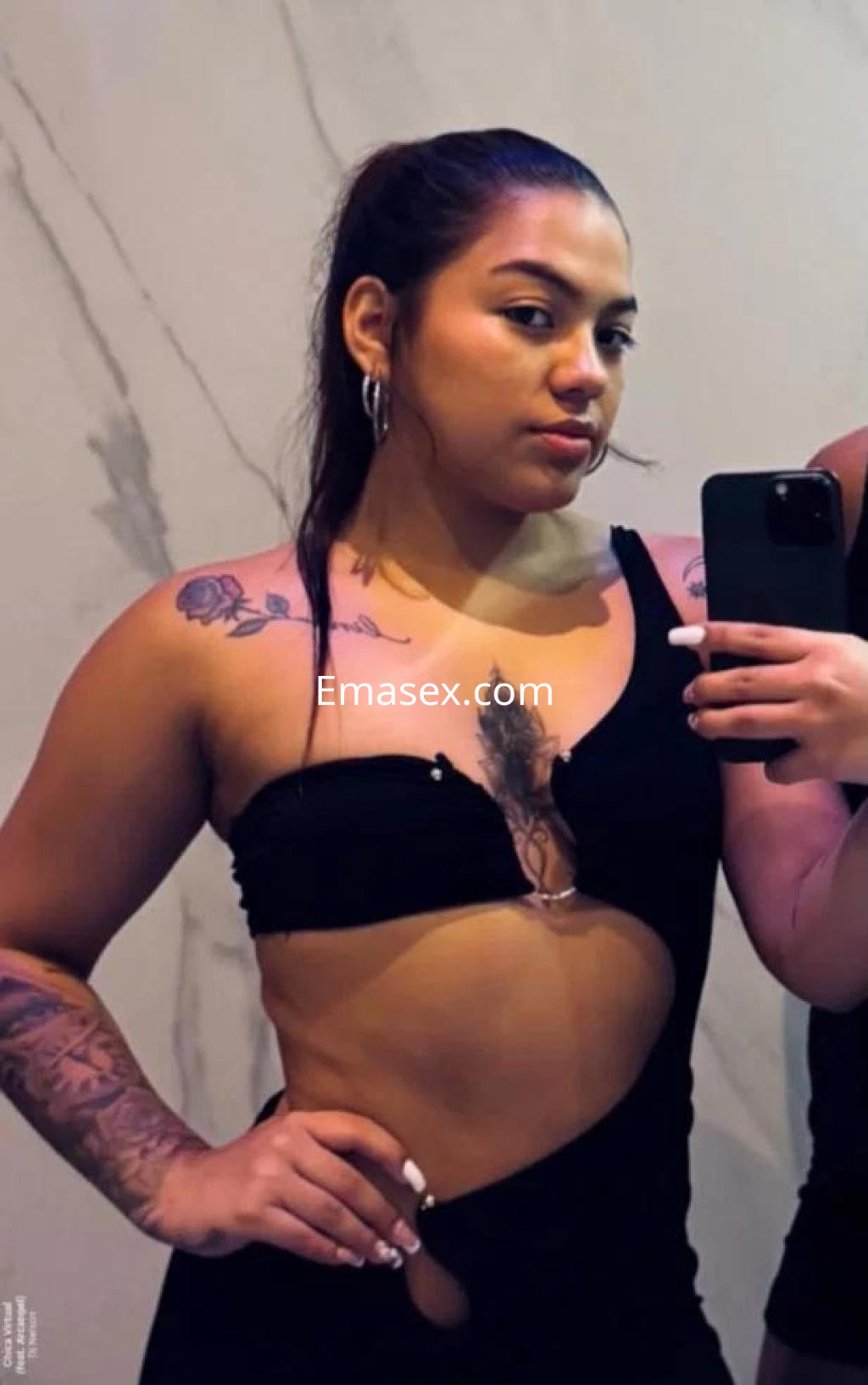 Escort en Salamanca con cabello recogido, luciendo un vestido negro ajustado y tatuajes visibles.