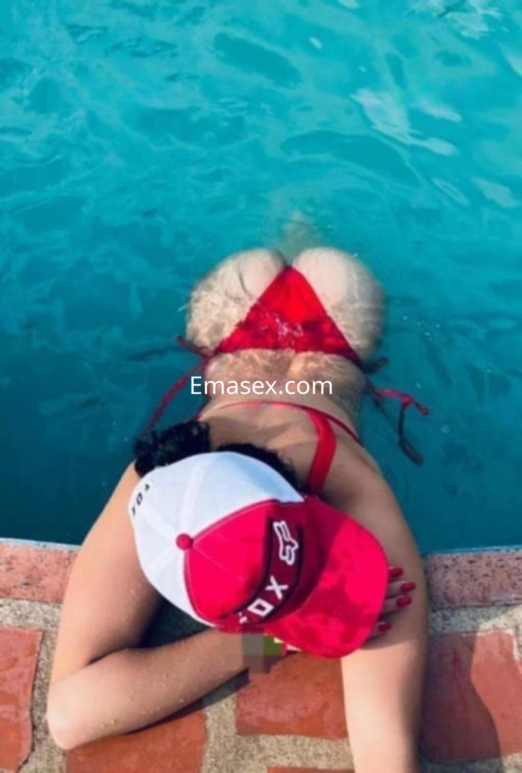 Escort en Cádiz luciendo un bikini rojo mientras se relaja en la orilla de una piscina, con una gorra blanca.