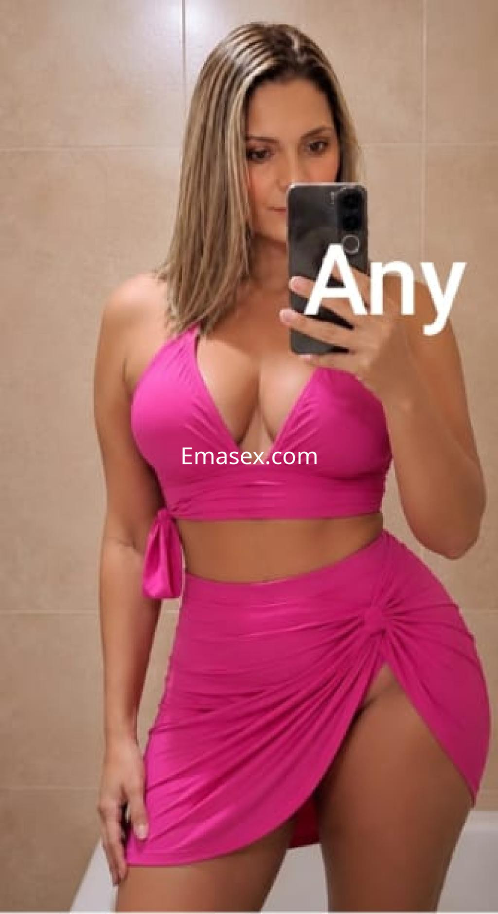 Escort en Santiago con cabello rubio y lacio, viste un conjunto rosa que resalta su figura en un espejo.
