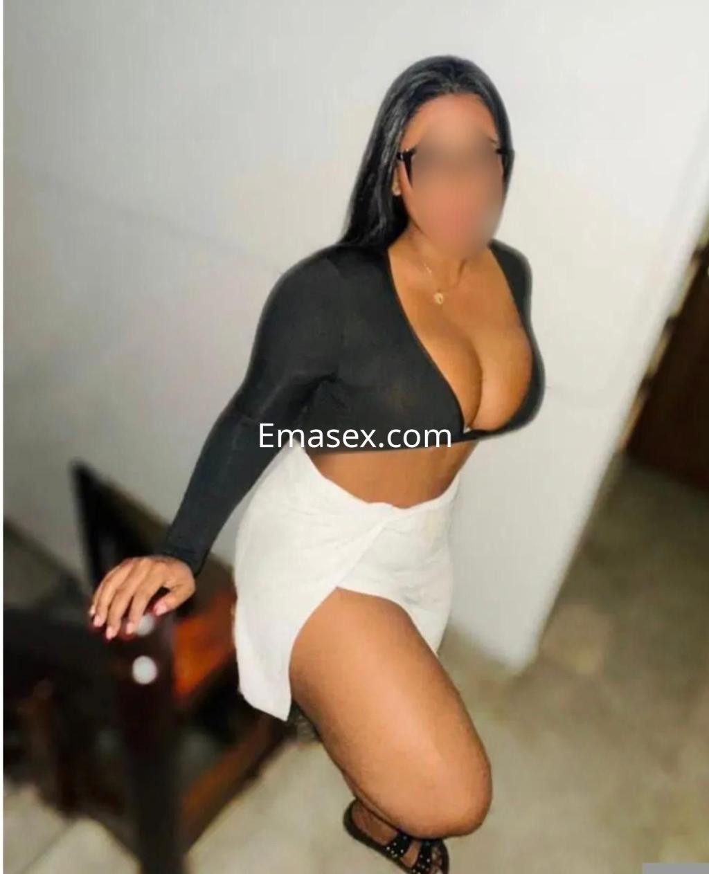 Escort en Málaga posando en una escalera, vistiendo un top negro de manga larga y una falda blanca, con cabello largo y lacio.