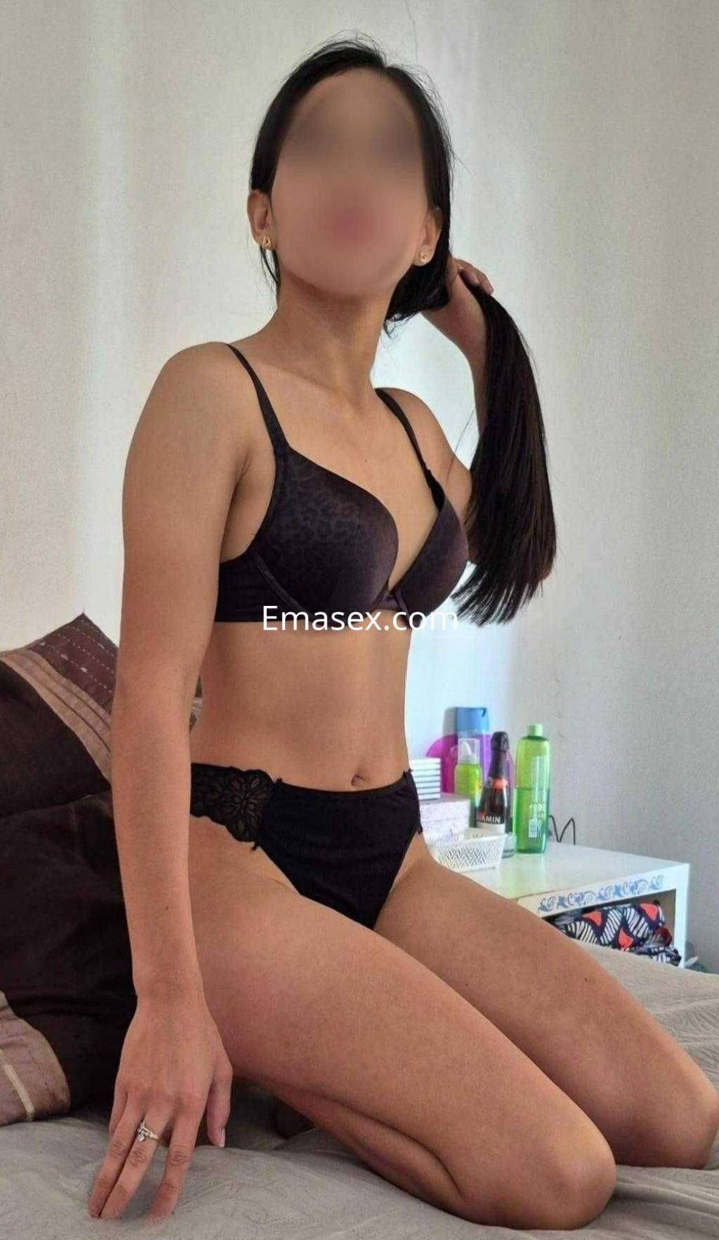 Puta de Madrid sentada en la cama, vistiendo sujetador negro y braguitas, con el pelo largo y liso.