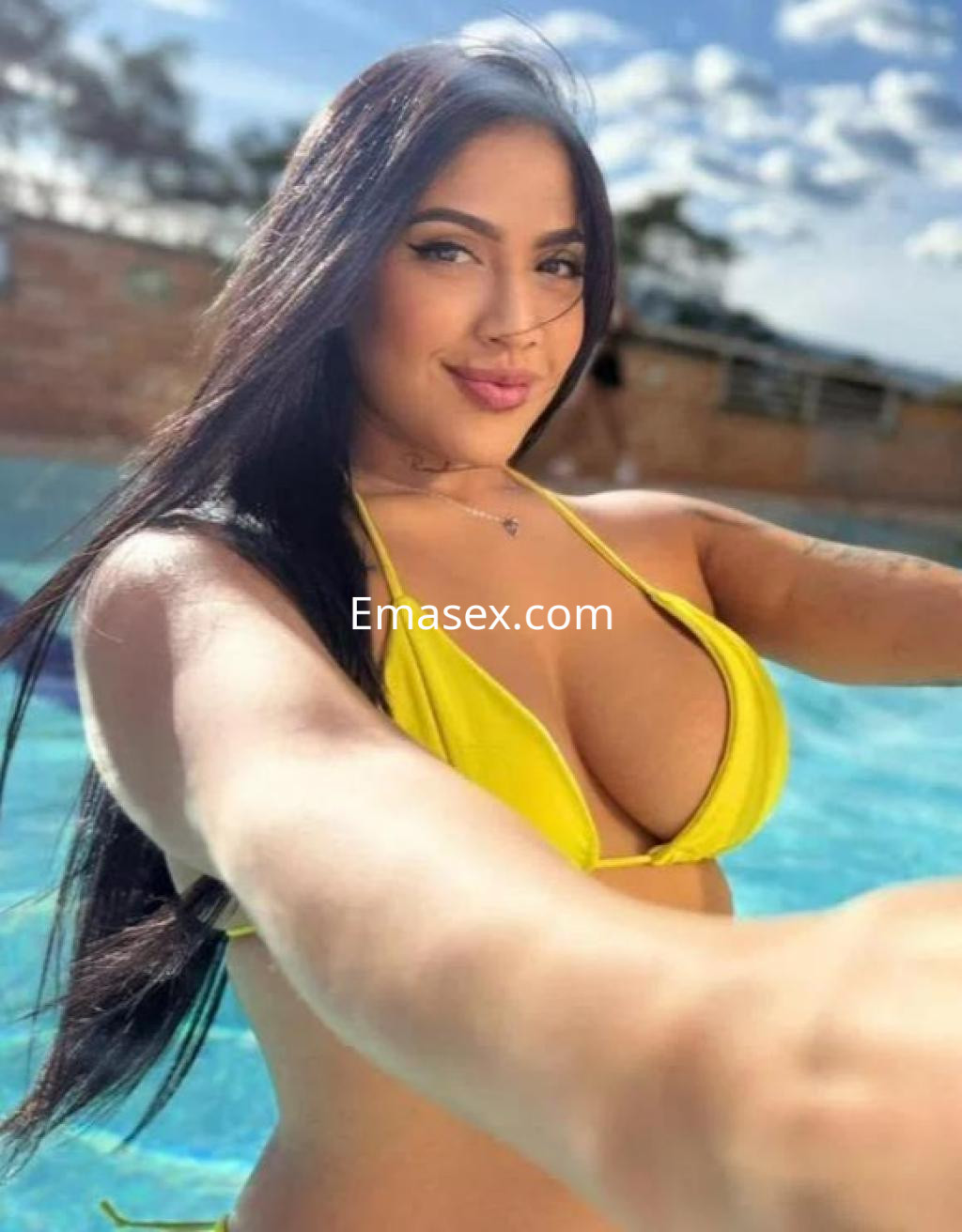 Escort con cabello largo y oscuro, usando un bikini amarillo mientras posa junto a la piscina en Barcelona.
