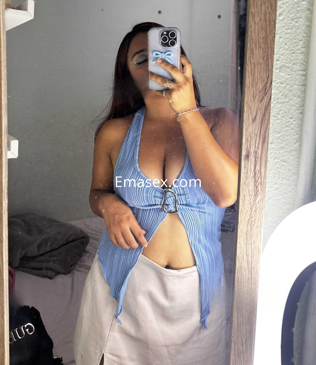 Escort en Barcelona, reflejada en un espejo, vistiendo una blusa de rayas azul y una falda corta clara.