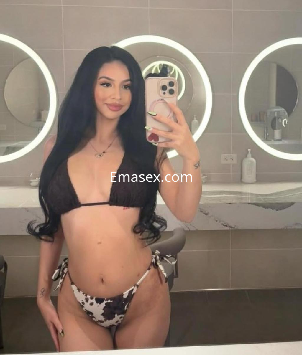 Escort en Huelva se muestra en un baño moderno con un bikini de estampado de vaca y cabello largo y ondulado.