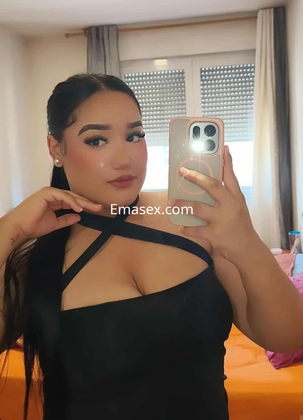 Escort en Pamplona con cabello largo y lacio, viste un vestido negro con tiras cruzadas mientras se toma un autorretrato.