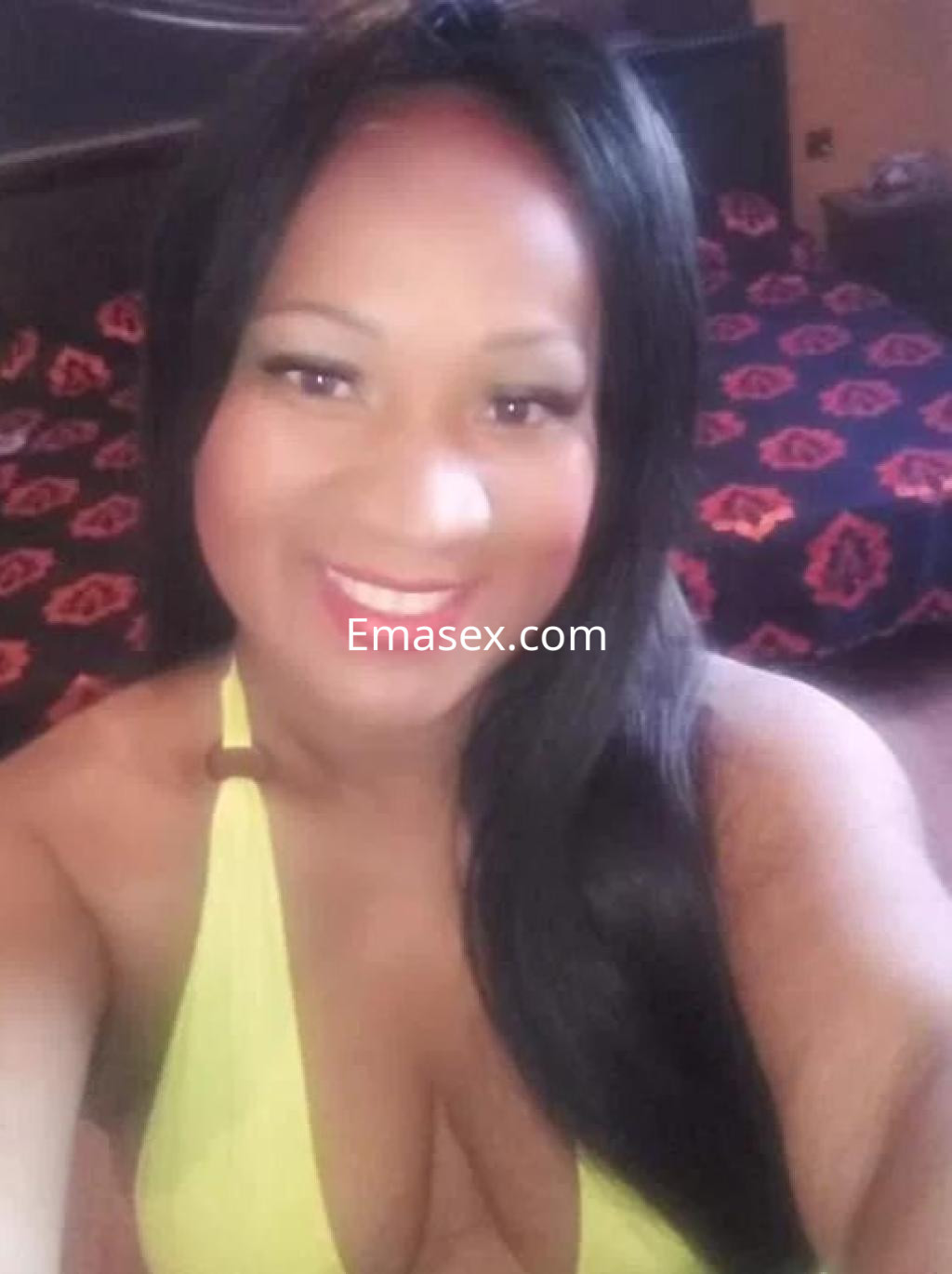La escort de Almería sonríe mientras lleva un bikini amarillo, en un entorno con fondo de cama oscura.
