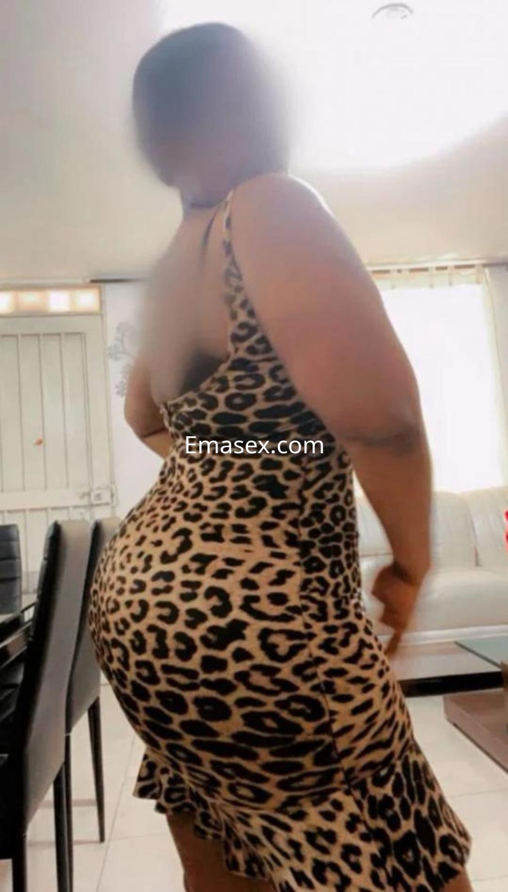 Puta de León posando de perfil con un vestido ajustado de estampado de leopardo en un ambiente interior.