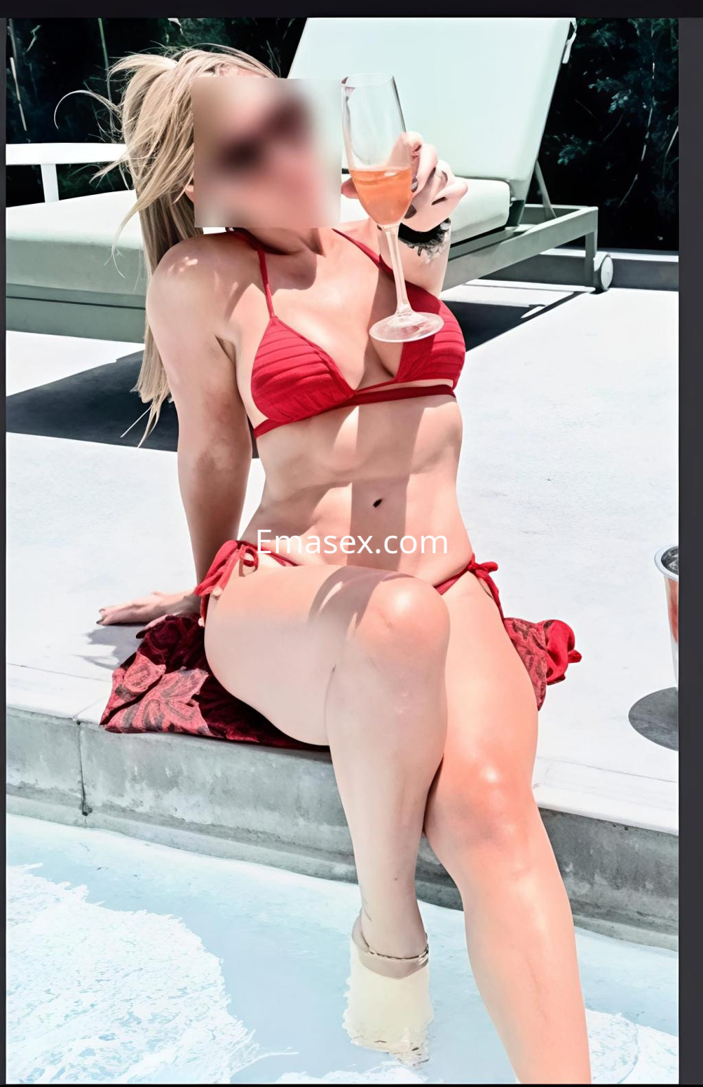 Escort en Salamanca sentada junto a una piscina, luciendo un bikini rojo y sosteniendo una copa de bebida.