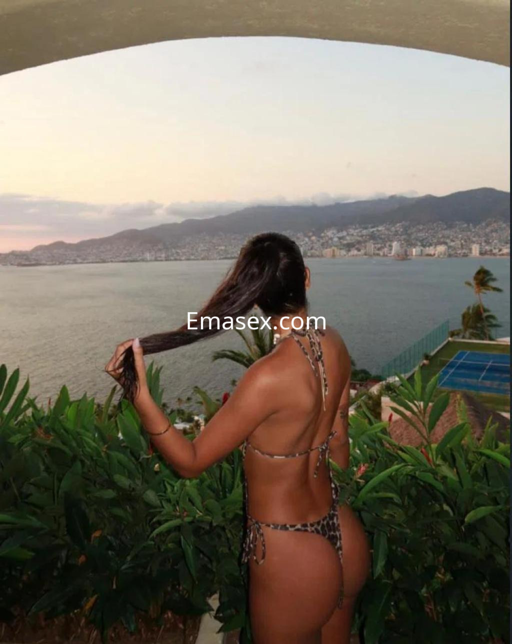 La puta viste un bikini de animal print y posa de espaldas ante un paisaje costero en Málaga.