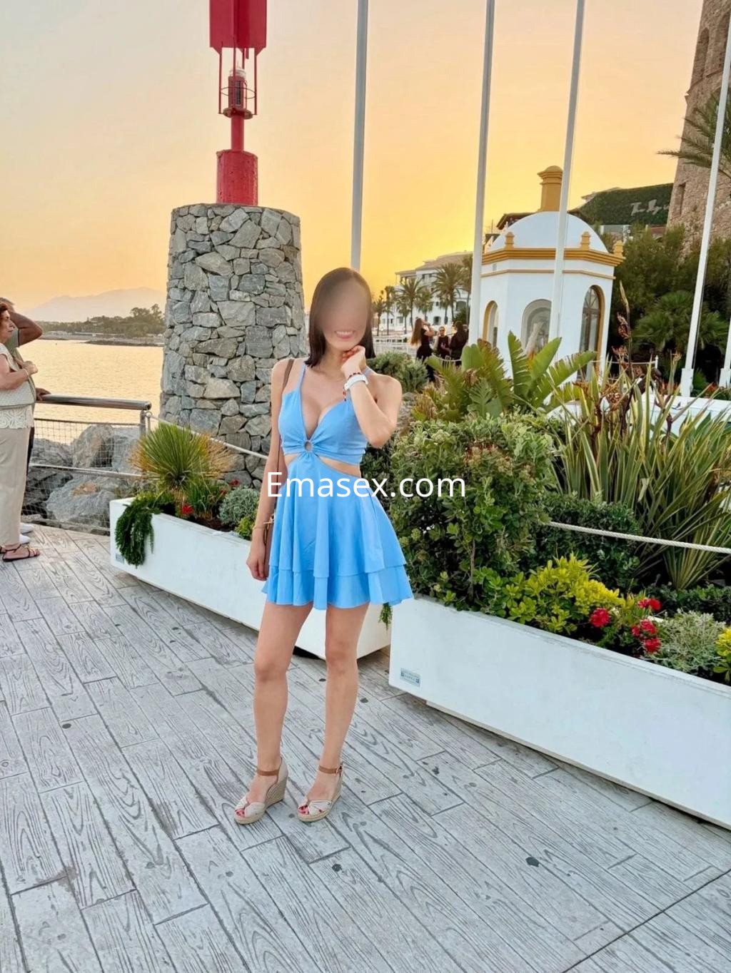 Puta en Coruña viste un vestido corto azul, posando con un fondo de mar y atardecer.