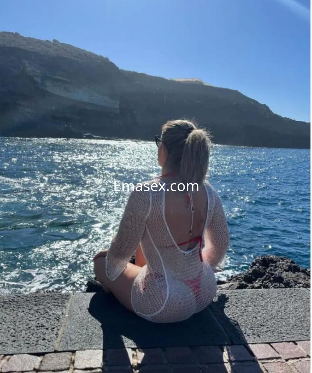 Escort sentada en un muelle de Santander, luciendo un traje de baño rojo y un cover up blanco, mirando al mar.