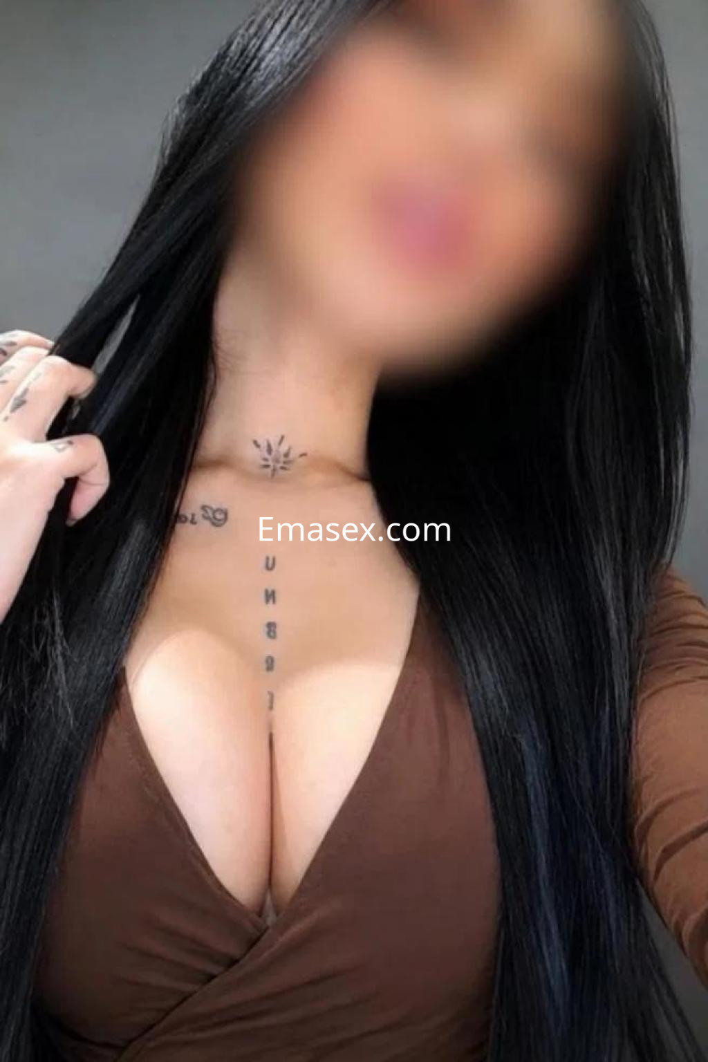 Escort en Valladolid luce un vestido marrón escotado, con cabello largo y lacio, mostrando un tatuaje en el pecho.