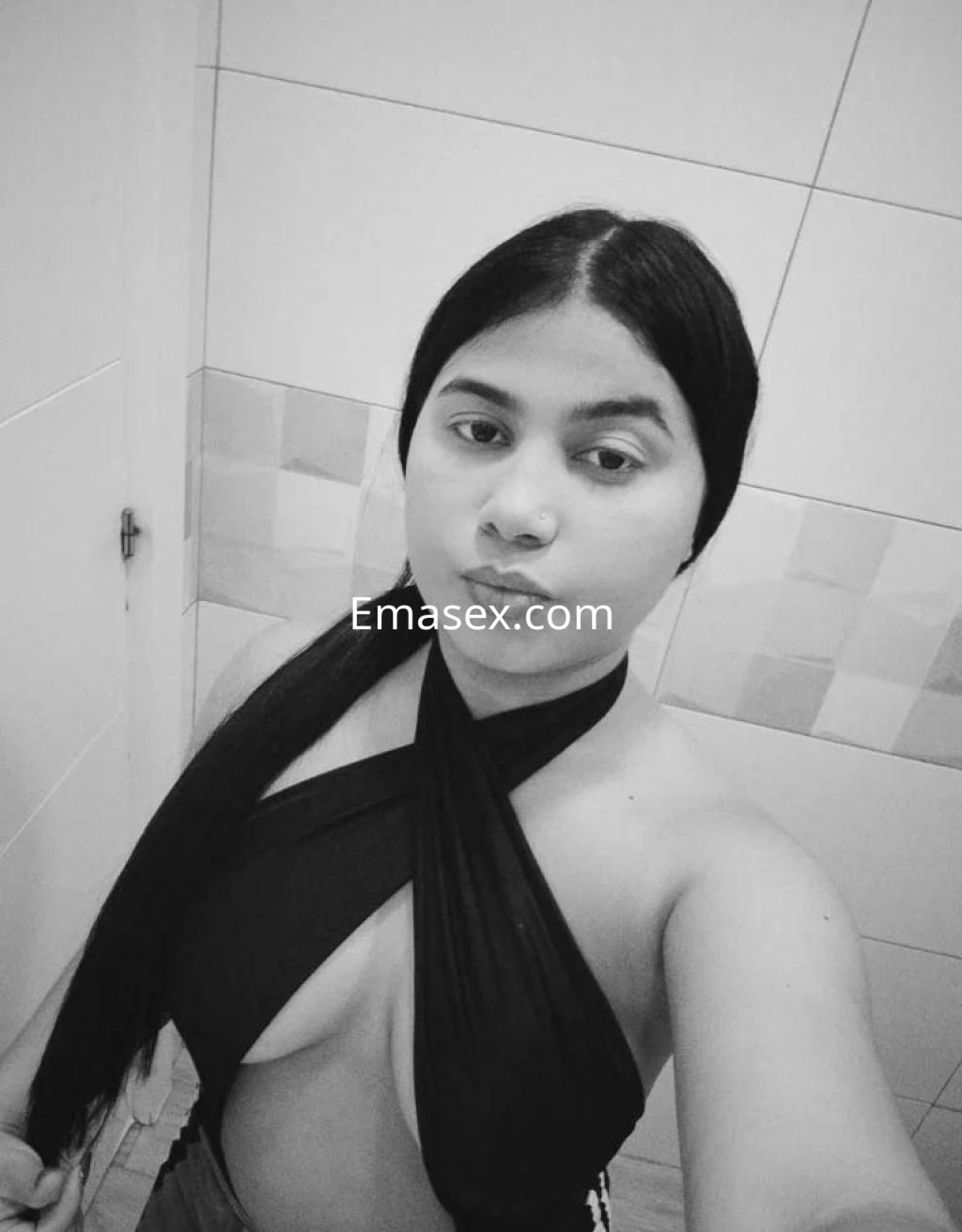 Puta en León, posando con un top negro que resalta su figura y cabello largo, en un ambiente de baño.