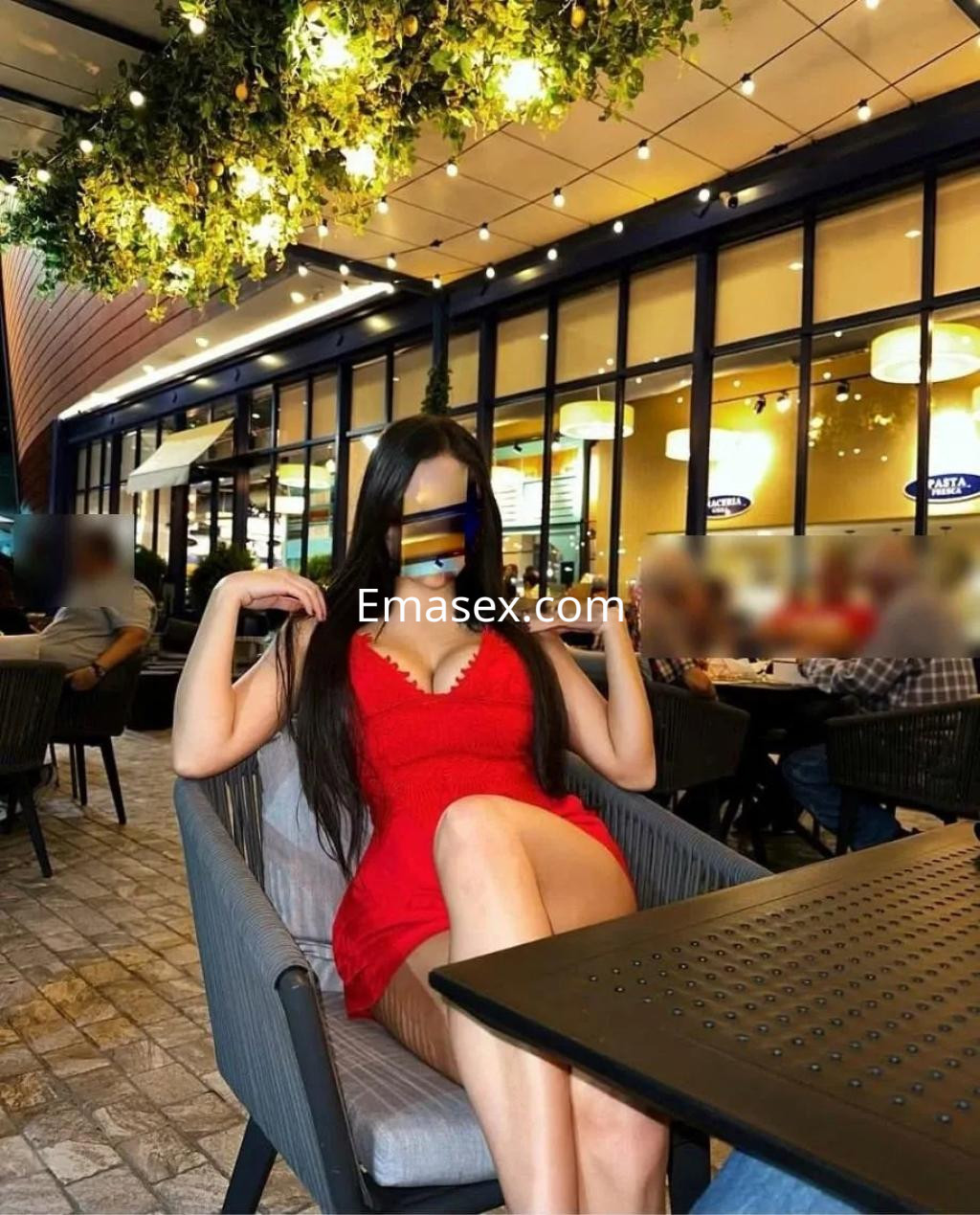 Puta con vestido rojo ajustado, sentada en una terraza en Albacete, mostrando su figura en un ambiente acogedor.